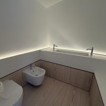 Corner bathroom installation: a Corian worktop with a washbasin trough, a wall-hung bidet and whitewashed timber cabinets