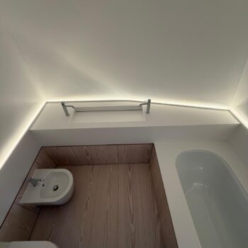A continuous Corian worktop running from the washbasin area into the bath surround, lit by a linear LED strip