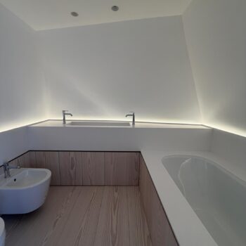 Loft bathroom with a sloping ceiling, a Corian washbasin trough and an undermounted bath in a surround made from the same material